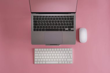 Fare ve klavyeli dizüstü bilgisayar. Üst manzara pembe renkli masa. Boş temiz arkaplan.