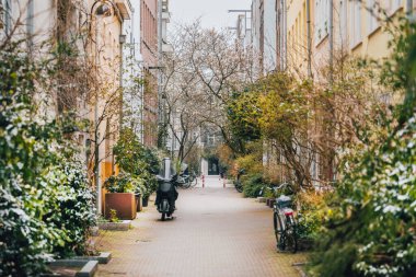 Yeşillikleri olan küçük bir şehir caddesi. Park edilmiş bisikletler ve motosikletler. Mimarlık ve yaşam tarzı.