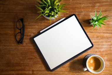 Tablet masada yatıyor. Temiz beyaz ekran modeli. Yukarıdan. Çiğ ahşap yüzey yeşil bitkileri.