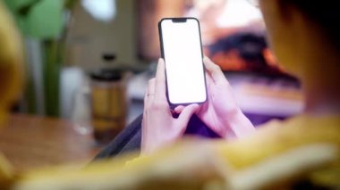 Kanepedeki kadın akıllı telefonu boş beyaz ekran maket ev oturma odası şöminenin iç tarafı televizyon masa yeşil bitki.