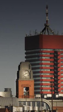 Arka planda modern bir gökdelenle çevrili, hızlı hareket eden elleri olan bir saat kulesinin dikey zaman atlaması.