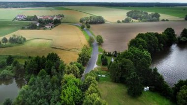 Kırsal Yol Yaz Tarlaları Forest Lake Aerial. Orta Polonya 'da asfalt yolu, renkli tarlalar, orman kenarı ve insansız hava aracından görüntülenen su yüzeyi ile kırsal alan.