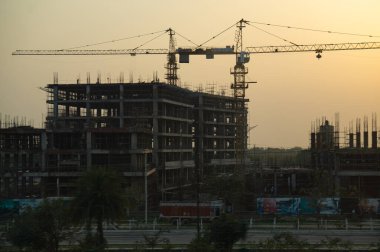 A large building is under construction and has two large cranes.