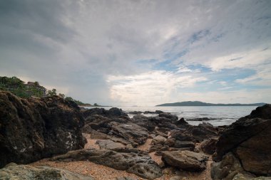 Deniz kenarındaki kayalar ve yağmur bulutları. Arkasında Koh Samet, Tayland.