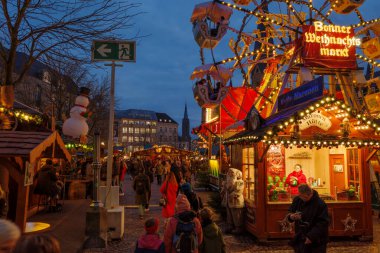Bonn, Almanya - 6 Aralık 2023: Kalabalık bir Noel pazarında kalabalık bir acil çıkış tabelasının alacakaranlık manzarası, festival ışıkları ve dekorasyonları, alışveriş yapan ve tatil atmosferinin tadını çıkaran ziyaretçiler.