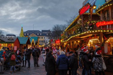 Bonn, Almanya - 6 Aralık 2023: Şenlikli ışıklar, dekore edilmiş tezgahlar ve tatil alışverişçileri ile hareketli bir Noel pazarının alacakaranlık manzarası.