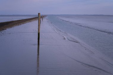 Neuharlingersiel 'deki limandan uzaklaşan seyrüsefer edilebilir bir kanal. Dalgalar çekildiğinde ve deniz tabanının etrafı aydınlandığında. Spiekeroog Almanya adası uzaktan görülebilir..