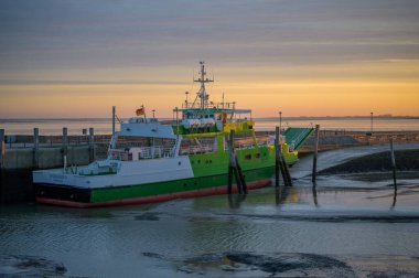 NEUHARLINGERSIEL, GERMANY - 26 Kasım 2022: Yolcu ve kargo feribotu Spiekeroog IV yanaştı ve alçak gelgitte kumda otururken liman kuru ve alüvyon halihazırda ferihazırda feribot altında görülebiliyor.