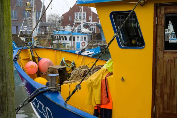 NEUHARLINGERSIEL, ALMANY - 26 Kasım 2022: Renkli mavi ve sarı köprü ve limandaki bir balıkçı teknesinin ön güvertesi