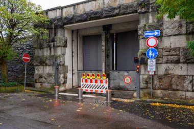 Ağır çelik kapılardan oluşan sel korumalı bariyer ve taşa yerleştirilmiş elektronik erişim bariyeri Alman bisiklet ve yaya levhalarının yanında..