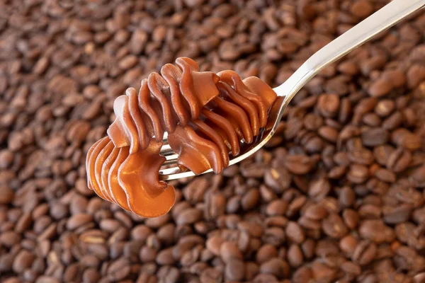 Close-up of coffee pasta on a fork against a background of coffee beans