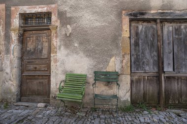 Old green chairs in the street against a wall