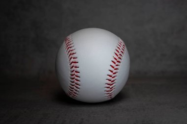 Gri arka planda kırmızı dikişli beyaz bir beyzbol topunun yakın çekimi