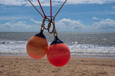 Arka planda deniz ve kumsal olan iplerden sarkan kırmızı tekne kılıfları.