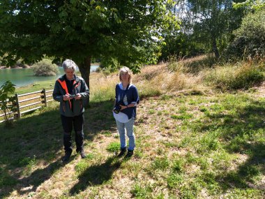 Bir adam uzaktan kumandalı kumandayı kontrol eder. Yanında kamera tutan bir kadın vardır.