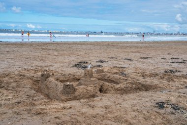 A sandcastle on a beach in Brittany with the sea in the distance and people swimming clipart