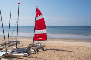 Brittany 'de kumlu bir sahilde, kırmızı ve beyaz yelkenli bir katamaran