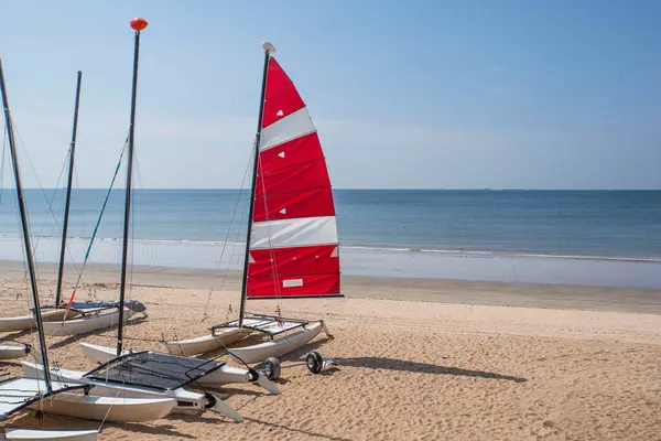Brittany 'de kumlu bir sahilde, kırmızı ve beyaz yelkenli bir katamaran