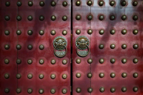 Traditional red wooden Chinese doors with brass lion head door knockers and ornamental studs.
