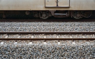 Tren vagonunun alt kısmı çakıllı tren raylarında tekerlekleri gösteriyor, yanında da boş bir tren yolu var..