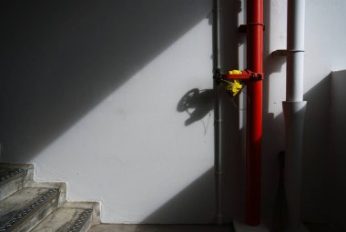 Kırmızı yangın musluğu borusunda sarı valf ve beyaz bir merdiven boşluğu var. Güçlü gölge ve karamsar.