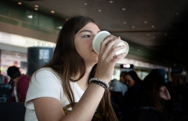 Young girl drinking coffee while waiting for her plane to depart clipart