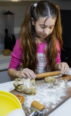 Evdeki mutfakta kurabiye yoğuran bir kız. Dikey yüksek kalite fotoğraf. Ulusal kurabiye günü. Yemek tarifi promosyonları için kullanılır. Çocukların yemek pişirme kavramı.