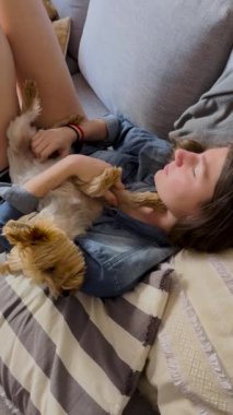 Yavru köpeğiyle rahatlamış bir kızın dikey görüntüsü. Sarışın kız yorkisiyle dinleniyor. Bedava yaşam tarzı konsepti. Sakin ve mutlu anlar. 