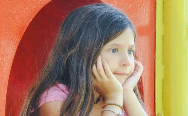 Kahverengi saçlı, açık renk gözlü, uzaktan izleyen küçük bir kız. Fotoğrafı kapat. Renkli bir geçmiş. Gerçek fotoğrafın yatay görüntüsü