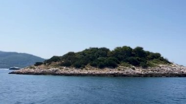 Issız ve engebeli bir adanın kıyılarını turlayan denizin güzel manzarası. Arka plan videosu. Mavi suyla çevrili egzotik bir adanın yüksek kaliteli yatay görüntüsü. Tatil temalı promosyonlar veya rahatlatıcı içerikler için ideal..