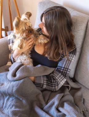 Genç bir kadın ve evcil hayvanı arasında parlak ve modern bir iç mekanda rahat bir etkileşimin dikey çekimi. Doğal ışık. İnsan ve evcil hayvan arasındaki duygusal bağ ve şefkat sahnesi..