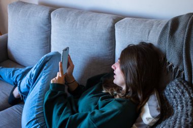 Güzel sarışın bir genç kanepede dinleniyor, rahat ve rahat, modern gençlik tarzı, samimi bir portre. Yazı için yer var. Gerçek yatay resim