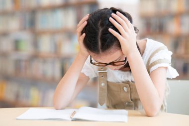 Asyalı kız kütüphanede ödev yapıyor. 