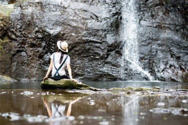 Şelalenin yanında oturan genç kadın. 