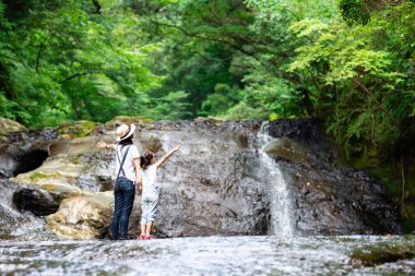 Anne ve kızı sabah ormandaki şelale manzarasının keyfini çıkarıyorlar.