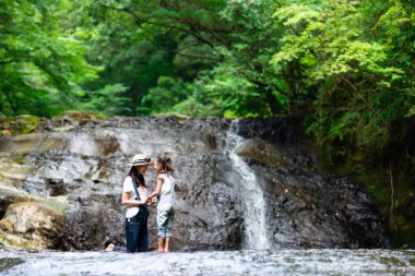 Anne ve kızı sabah ormandaki şelale manzarasının keyfini çıkarıyorlar.