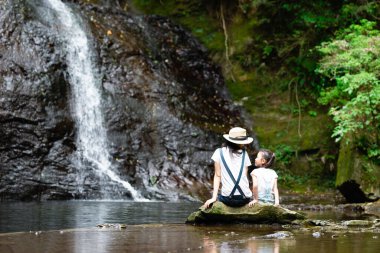 Anne ve kızı sabah ormandaki şelale manzarasının keyfini çıkarıyorlar.
