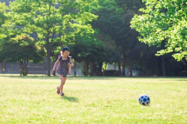 Küçük kız çimenlerde futbol oynuyor. 