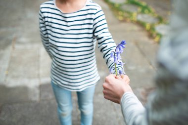 Bir çocuk ve anne elleri açık havada çiçek taşıyor.