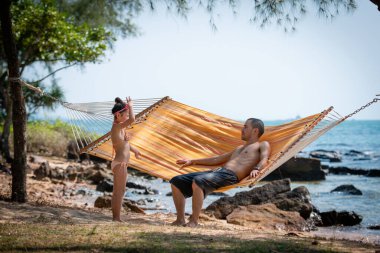 Baba ve kızı sahilde hamakta oynuyorlar.