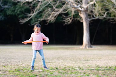 Asyalı kadın parkta hulahop oynuyor.