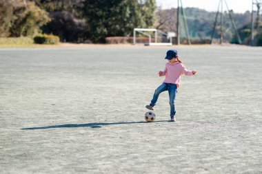 Çocuk kız parkta futbol topuyla oynuyor. 