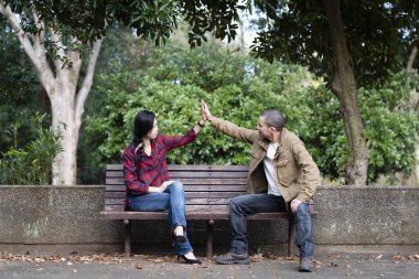 Genç çift parkta bir bankta beşlik çakıyor.