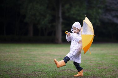 Sonbahar sezonunda yağmurluklu Asyalı kız ve şemsiyesi parkta.