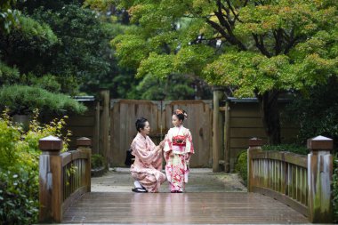 Genç Asyalı anne ve kızı geleneksel Japon elbiseleriyle köprüde. 
