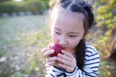 Asyalı kız dışarıda kırmızı elma yiyor.