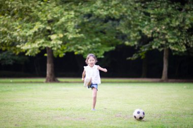 Küçük kız çimenlerde futbol topuyla oynuyor. 