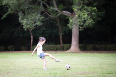 Küçük kız çimenlerde futbol topuyla oynuyor. 