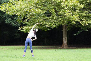 Genç Asyalı kadın parkta geriniyor.