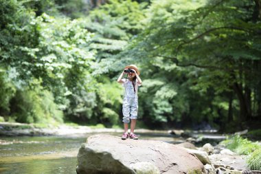 Nehir kenarında dürbün kullanan çocuk